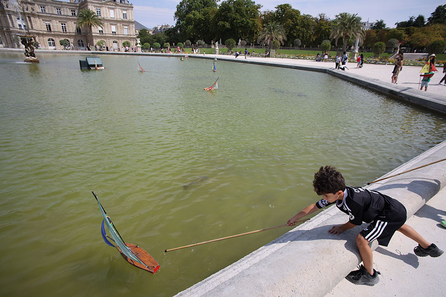 Photo of Small Boy Controlling a Model Sailboat With a Stick.